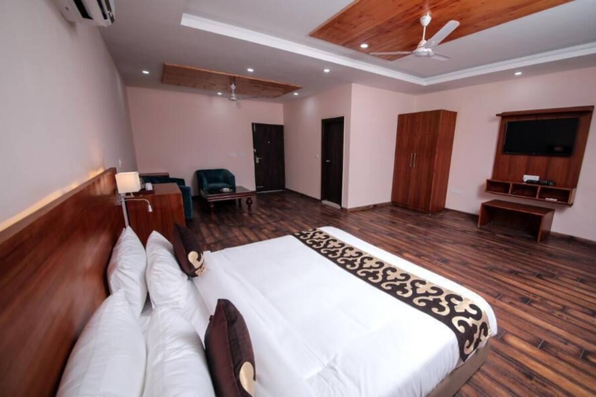 A hotel room with a large bed, wooden flooring, a ceiling fan, a TV, and a wardrobe.