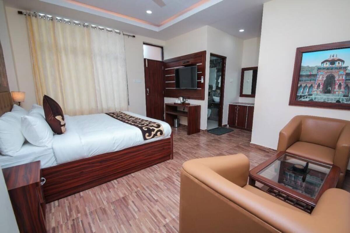 A hotel room with a bed, a sofa, a TV, a mirror, and a framed picture on the wall.