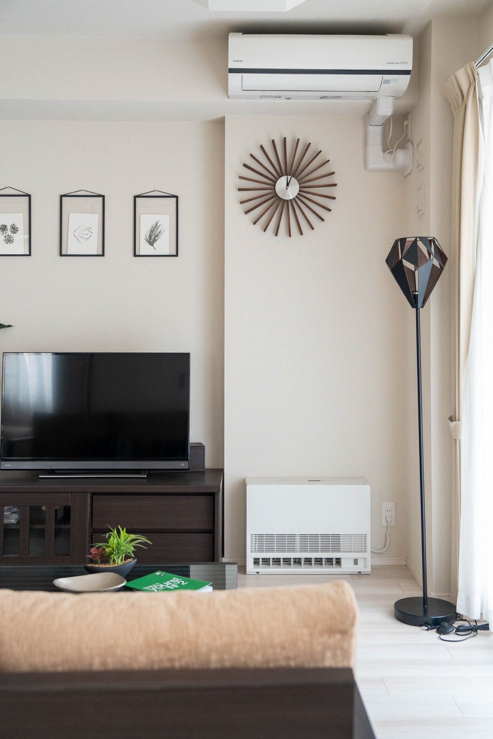 Een moderne woonkamer met een flatscreen-televisie, een decoratief kunstwerk, een staande lamp en een witte airconditioner.