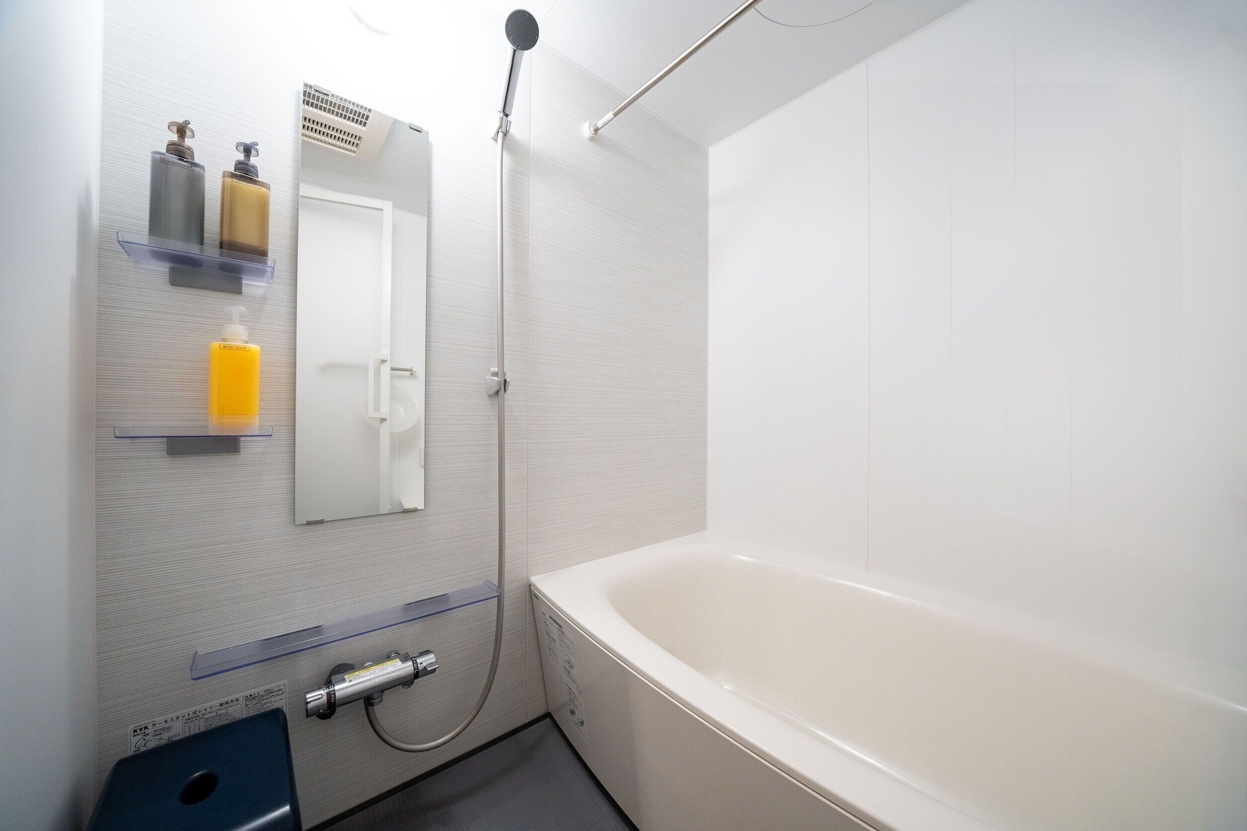 Une salle de bain moderne avec une baignoire blanche, une pomme de douche et des articles de toilette disposés sur une étagère fixée au mur.