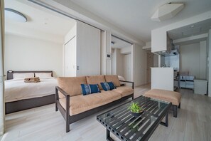 A modern hotel room with a sofa, a bed, a glass coffee table, and a kitchenette in the background. - MORGANITE 406 (Sapporo)