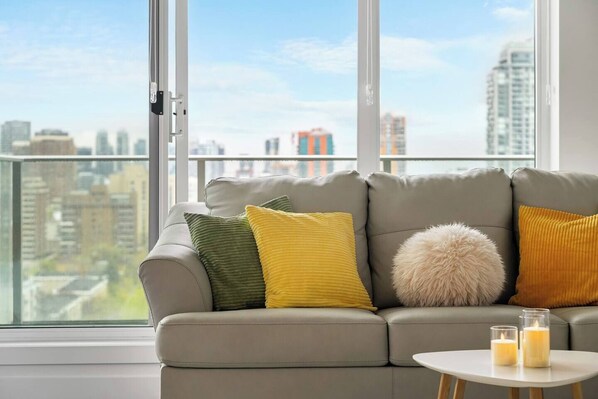 A grey sofa with three cushions in green, yellow, and white, and a fluffy white pillow. A small white table with two candles is in front of the sofa.