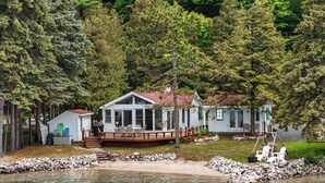 Un chalet au bord du lac, doté d’une terrasse et entouré d’arbres, avec une rive rocheuse.