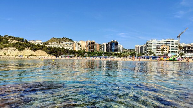 A beach with clear water, buildings in the background, and a hilly landscape. - CALA ALTA magic apartment (Benidorm)