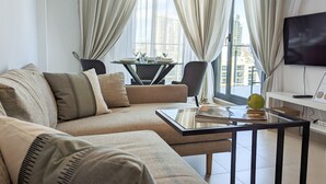 A modern living room with a sofa, a glass coffee table, a dining table with chairs, and a TV mounted on the wall. - CALA ALTA magic apartment (Benidorm)