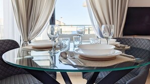 A dining table set with plates, glasses, and cutlery, surrounded by cushioned chairs, with a view of buildings through curtains. - CALA ALTA magic apartment (Benidorm)
