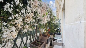 Een balkon met witte bloeiende planten, bloempotten en een kleine tafel met stoelen.