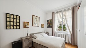 Een slaapkamer met een bed, nachtkastjes, een radiator en een raam met gordijnen.