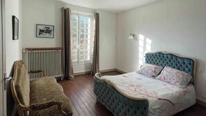 Ein Schlafzimmer mit Bett, Sessel, Heizkörper und einem fenster mit Vorhängen.