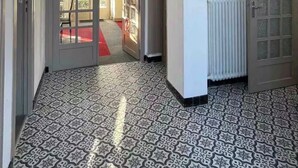 Ein Korridor mit gemusterten Bodenfliesen, einem Heizkörper und einer Tür zu einem anderen Raum.