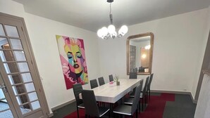 Ein Konferenzraum mit einem langen Tisch, Stühlen, einer Kandelaber, einem großen Spiegel und einem farbenfrohen Gemälde an der Wand.