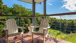 Terraza cubierta al aire libre con dos sillas Adirondack y una mesa pequeña con una botella y un vaso.
