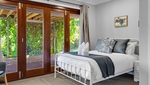 Un dormitorio con cama, mesita de noche, ventana con vistas a zonas verdes y puerta corrediza de vidrio que da a un espacio al aire libre.