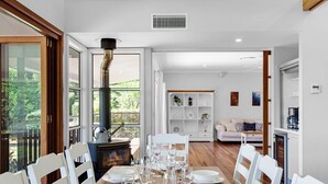 Comedor con mesa de madera dispuesta para seis personas, sillas blancas y un amplio ventanal con vistas al verdor.