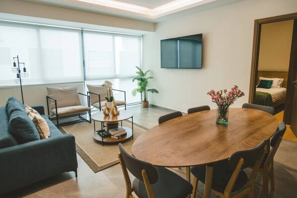 A modern living room with a round wooden dining table, a sofa, and a TV mounted on the wall. - Central, bright, cozy, and elegant Benci apartment (Ciudad de México)