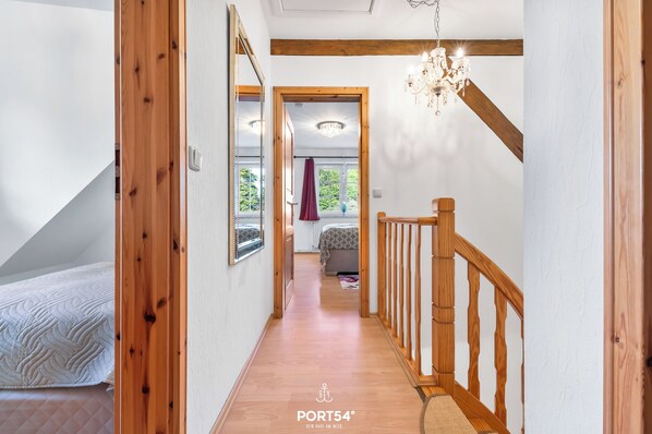 A narrow hallway with wooden flooring and a wooden railing. A chandelier hangs from the ceiling, and a bed is visible in the background. - Westerweide - terrace, fitness room, dogs allowed (Delve)
