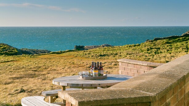 Une vue sur la côte, avec une table de pique-nique installée sur une colline herbeuse surplombant la mer.