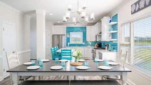 A modern kitchen with a dining area, featuring a large island, white cabinetry, and a blue backsplash. - The Saltwater Shack: Early Bird Special! (Oak Island)