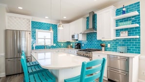 A kitchen with a central island, white cabinets, and blue-tiled backsplash. - The Saltwater Shack: Early Bird Special! (Oak Island)