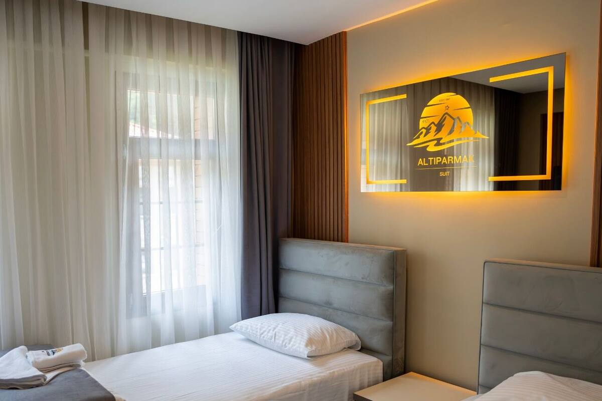 A hotel room with two beds, a large window with sheer curtains, and a wall-mounted sign with the hotel logo.