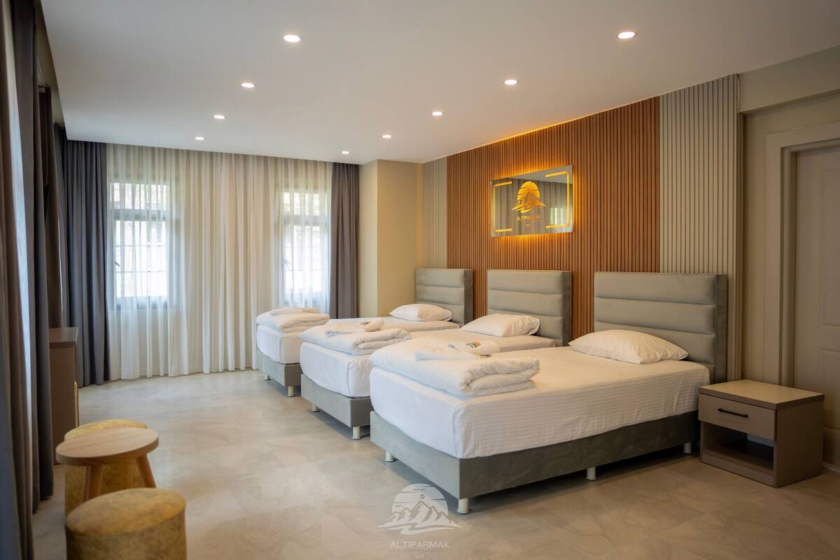 A modern hotel room with three beds, a wooden accent wall, and a large window with curtains.