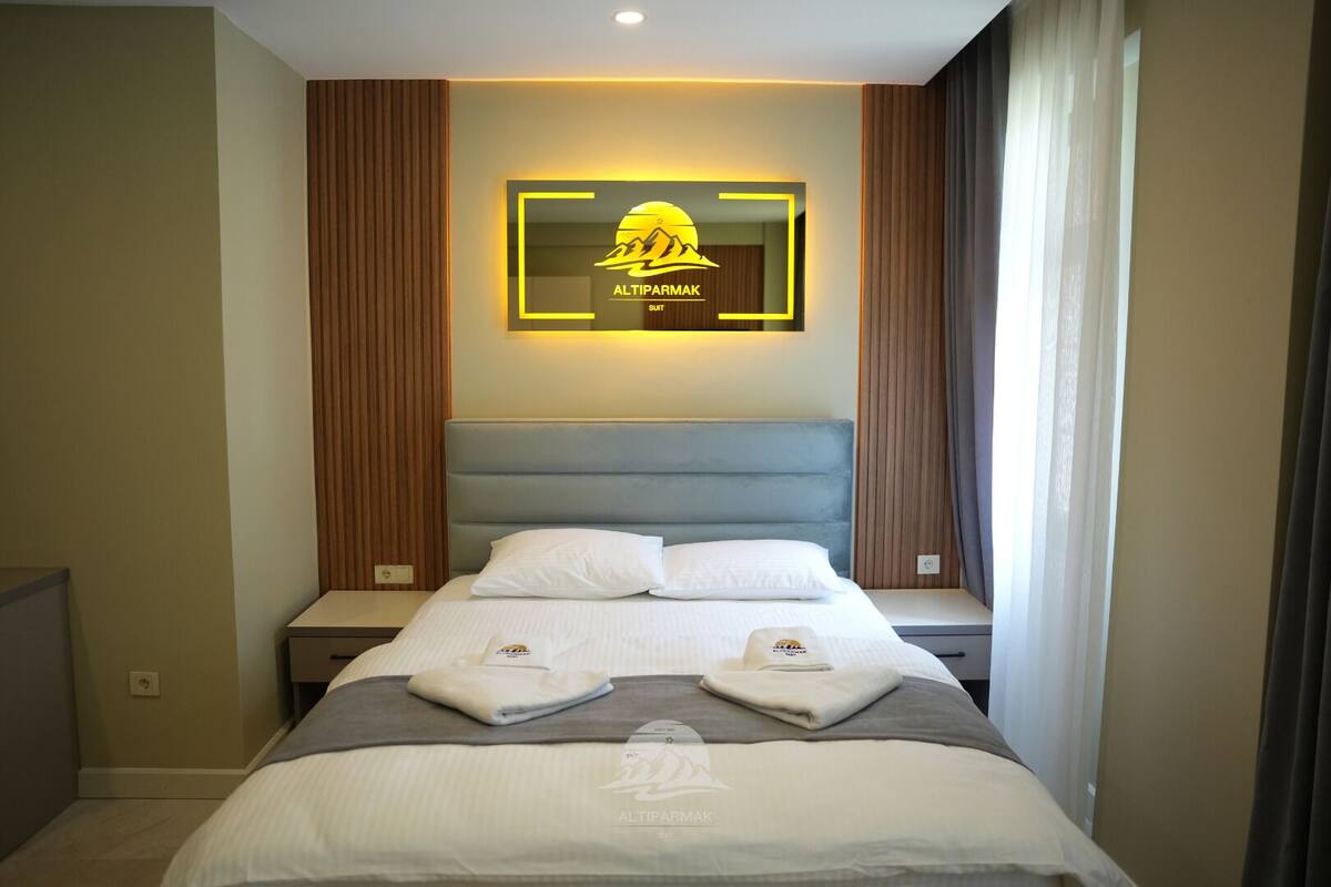 A hotel room with a bed, a headboard, a wall-mounted logo, and a window with curtains.