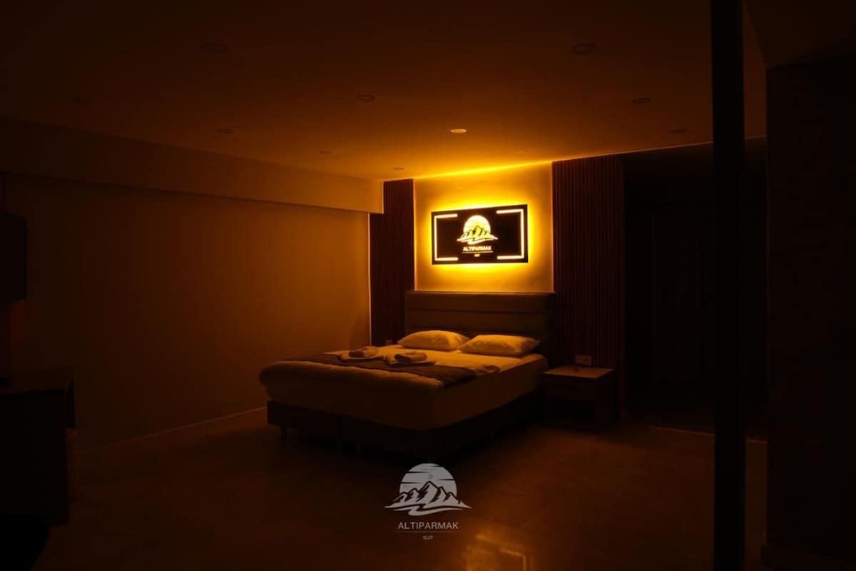 A dimly lit bedroom with a bed, a nightstand, and a wall-mounted TV.