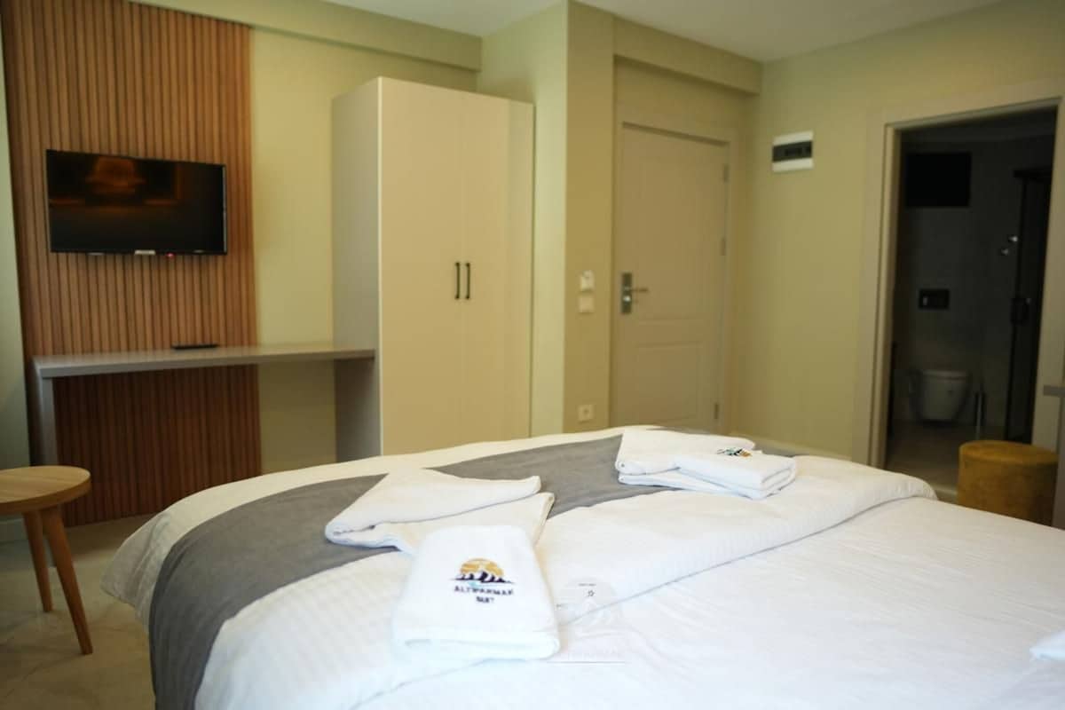 A hotel room with a bed, a TV mounted on a wooden panel wall, a wardrobe, and a door leading to a bathroom.