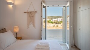 Un dormitorio con cama, una mesita de noche con lámpara, un colgador de macramé y vistas al exterior.