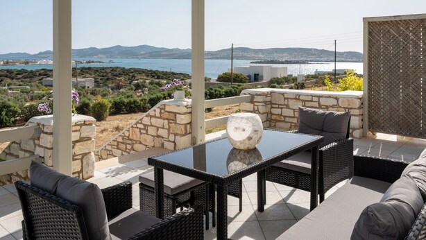 Un espacio de estar al aire libre techado, con paredes de piedra, una mesa con cubierta de vidrio y muebles de mimbre.