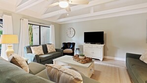 Ein Wohnzimmer mit Deckenventilator, einer Couch, einem Couchtisch, einem Fernseher und einer Wanduhr.