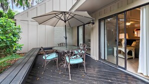 Eine Terrasse im Freien mit Tisch, Stühlen und einem Sonnenschirm, sowie eine Glastür zu einem Innenbereich.