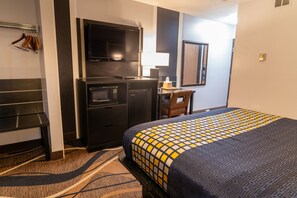 Une chambre d’hôtel équipée d’un lit, d’un bureau, d’une télévision, d’un four à micro-ondes et d’un porte-manteau.