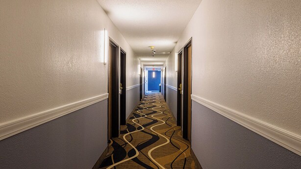 Ein Hotelgang mit Teppichmuster, weißen Wänden und Türen an beiden Seiten.