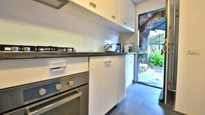 A modern kitchen with white cabinets, a stainless steel stove, and a view of a garden through an open door.