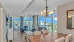 A spacious room with a wooden dining table, a sofa, and a ceiling fan. - 2BR Penthouse End Unit w/ Indoor Waterparks! (Myrtle Beach)