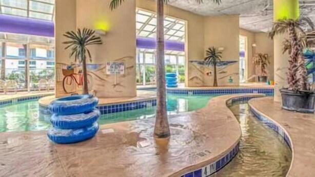 An indoor swimming pool with multiple lanes, palm trees, and a tropical mural on the walls. - 2BR Penthouse End Unit w/ Indoor Waterparks! (Myrtle Beach)