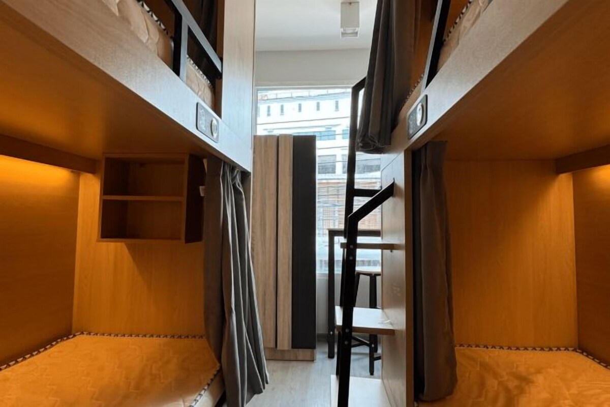 Una habitación pequeña y estrecha, con muebles de madera, literas, una mesita y una silla.