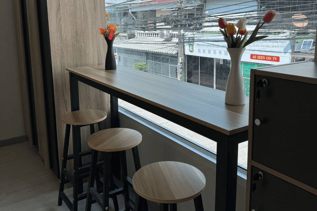 Una cocina moderna con encimera de madera, dos taburetes y vista a un paisaje urbano a través de un amplio ventanal.