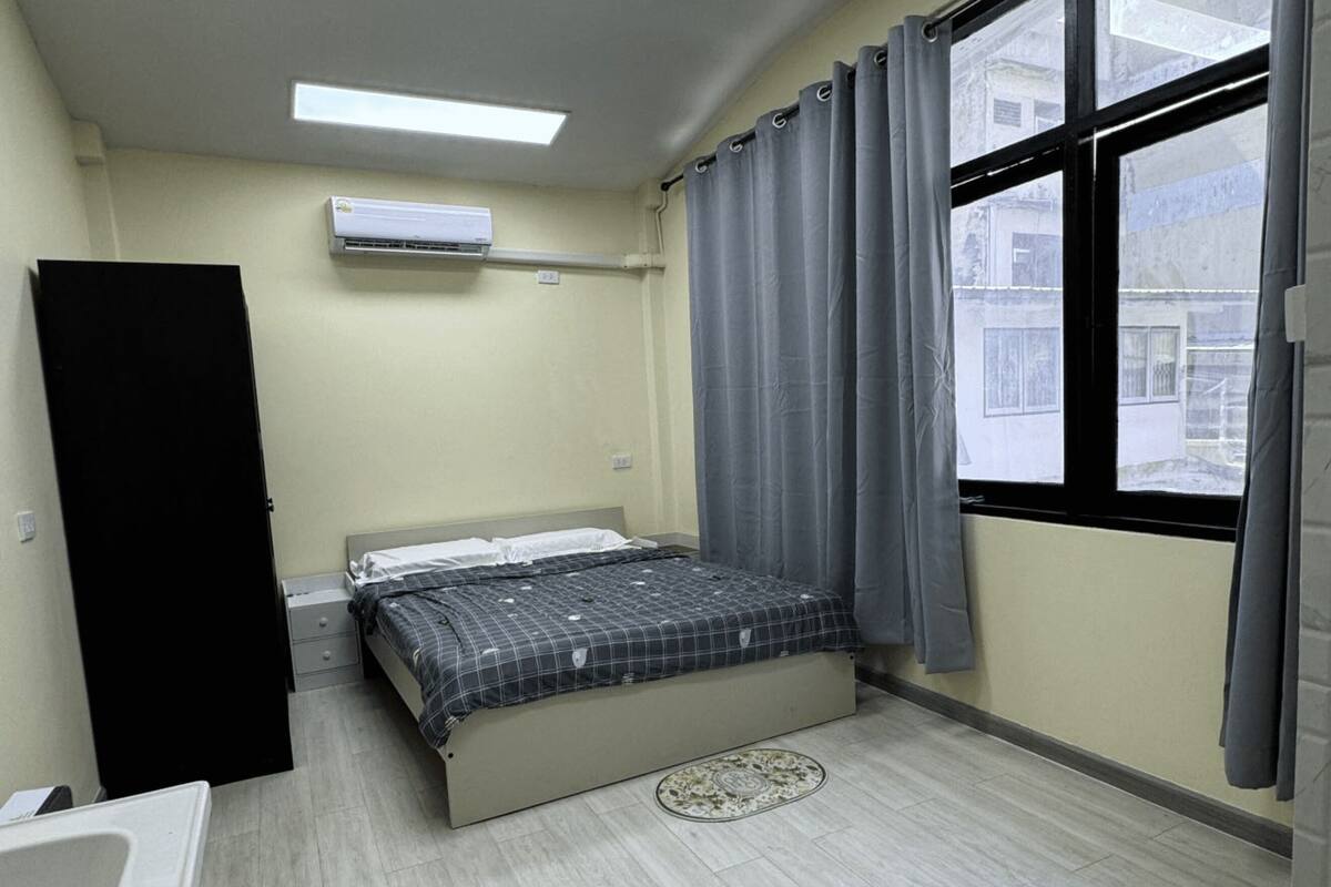 Un dormitorio con cama, ventana con cortinas, equipo de aire acondicionado y baño con lavamanos.