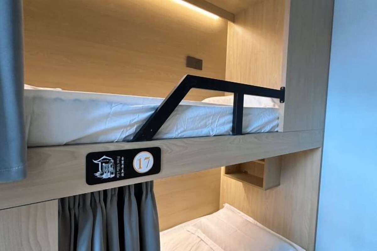 Una cama litera con cabecera identificada con el número 17 y un estante pequeño debajo.