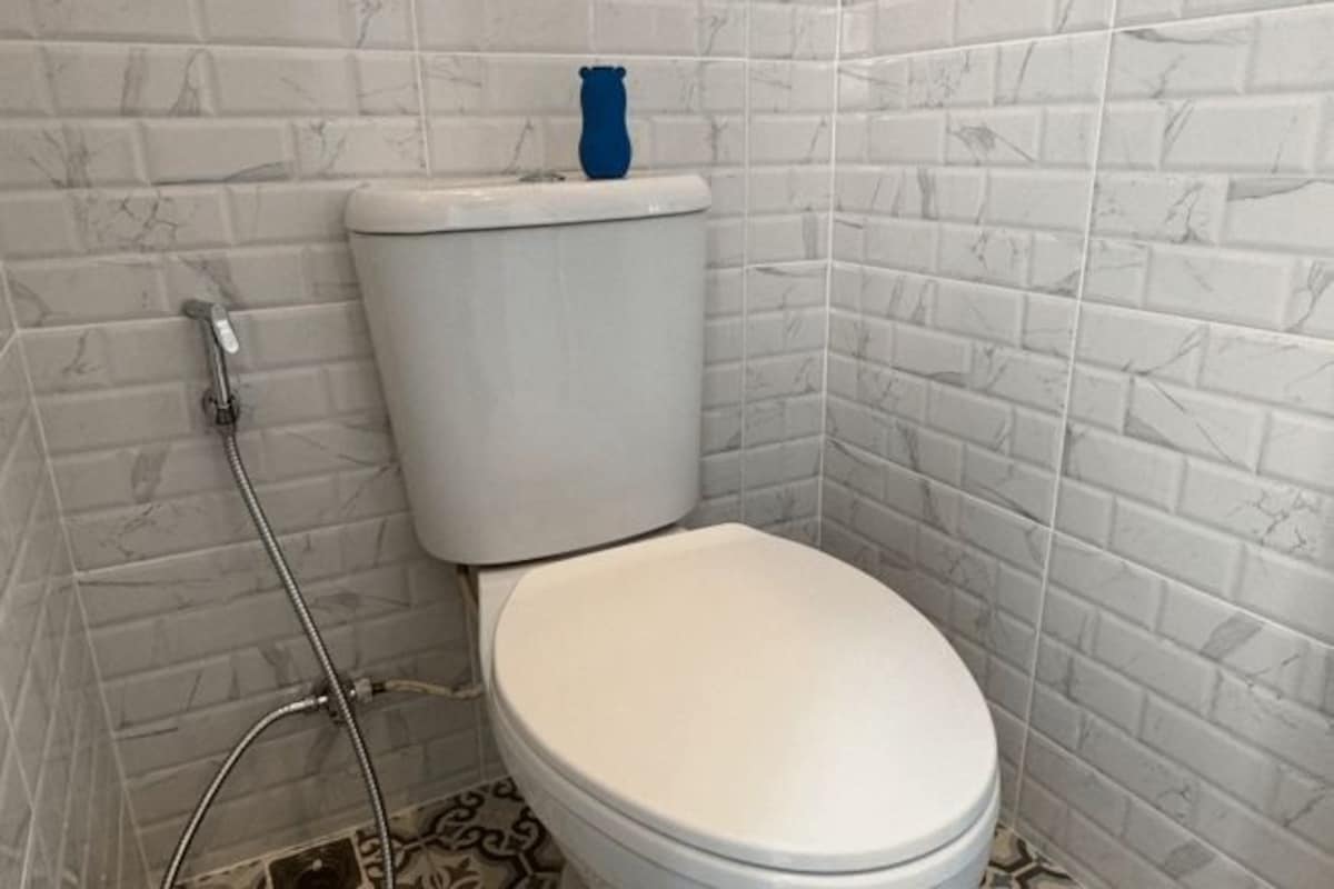 A bathroom with a white toilet, a blue vase on the tank, and patterned floor tiles.