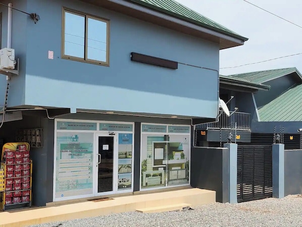 Un bâtiment à la façade bleue, doté d’une entrée sécurisée par un portail et d’une enseigne publicitaire pour des services d’ingénierie.
