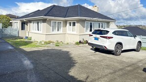 A single-story house with a dark roof, a white car parked in the driveway, and a clear blue sky with clouds.