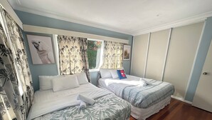 A hotel room with two beds, floral curtains, a Spiderman pillow, and a framed picture on the wall.