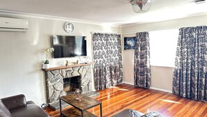 A living room with a stone fireplace, leather sofa, wooden flooring, and patterned curtains.