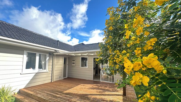 A house with a wooden deck, a garage, and a garden with yellow flowers.