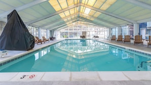An indoor swimming pool with a covered roof, clear glass walls, and wooden lounge chairs around the pool. - 2BR Near Beach | Bay Views + Jolly Roger Fun (Ocean City)