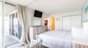 A bedroom with a large bed, a dresser, a TV mounted on the wall, and a sliding glass door leading to a balcony. - Ocean City State of Mind | Bayfront Views & Chill Vibes (Ocean City)