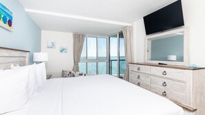 A hotel room with a large bed, a dresser, a TV, and a view of the sea. - Salty Air & Sunset Chairs | Bayfront Bliss in OCMD (Ocean City)